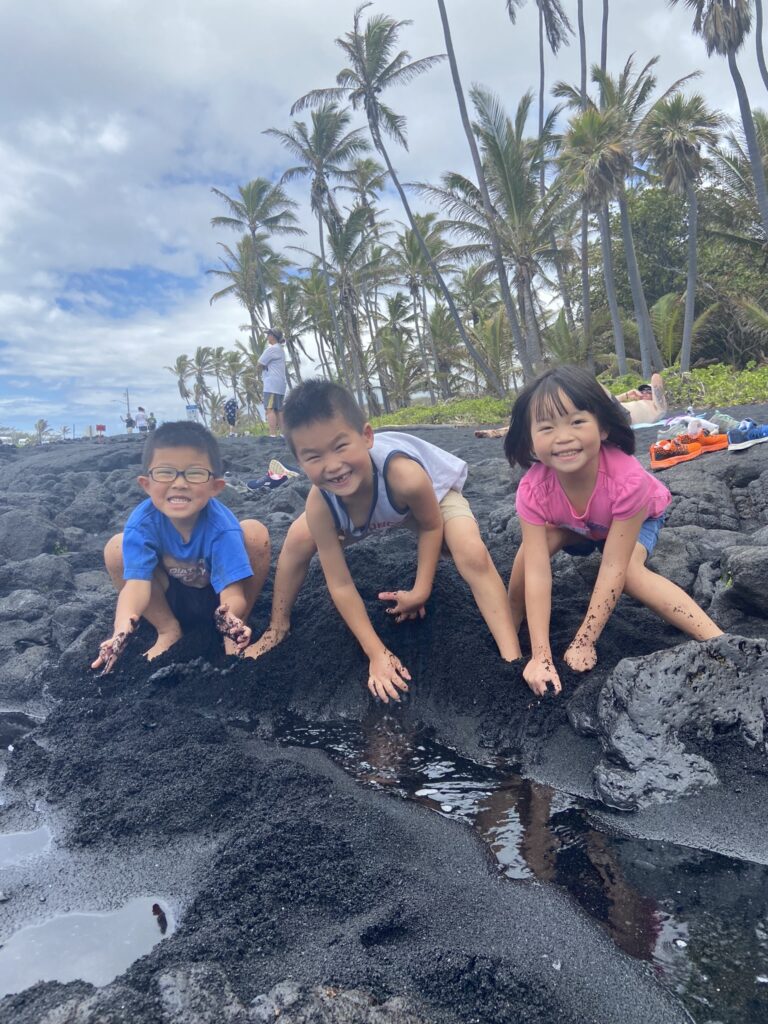 kids playing on a black sand beach in hawaii