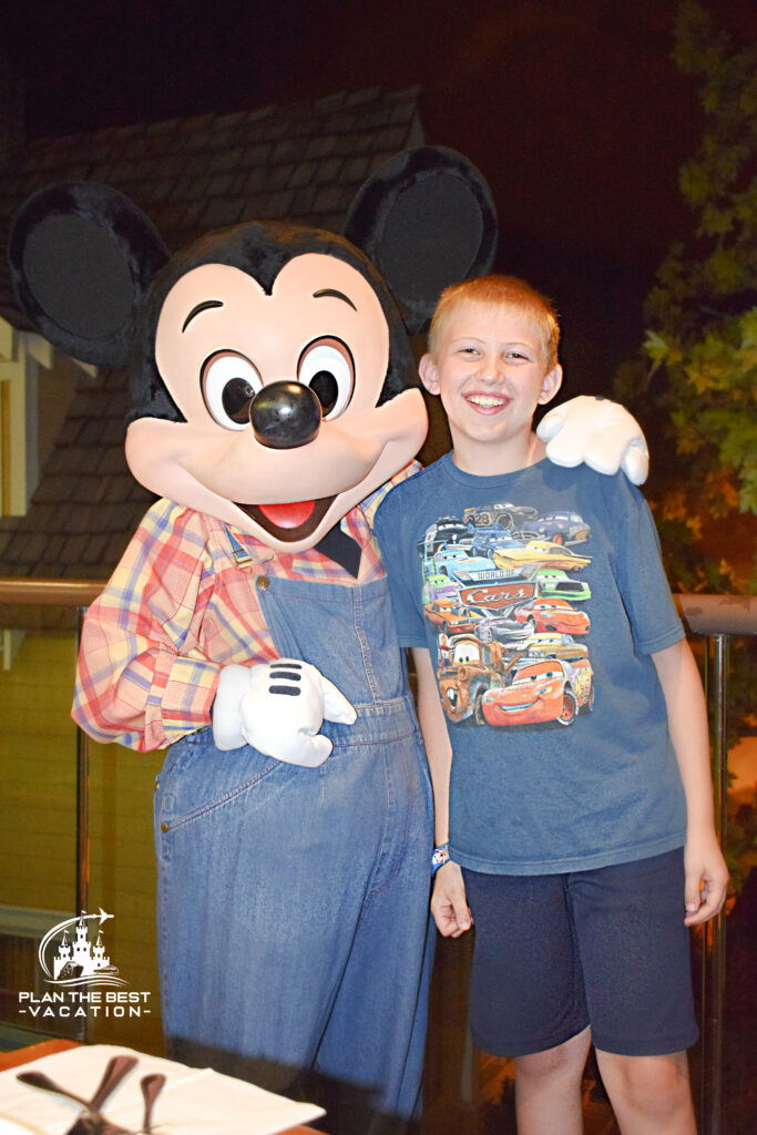 farmer mickey from garden grill restaurant at epcot in disney world with pre-teen boy wearing disney cars shirt