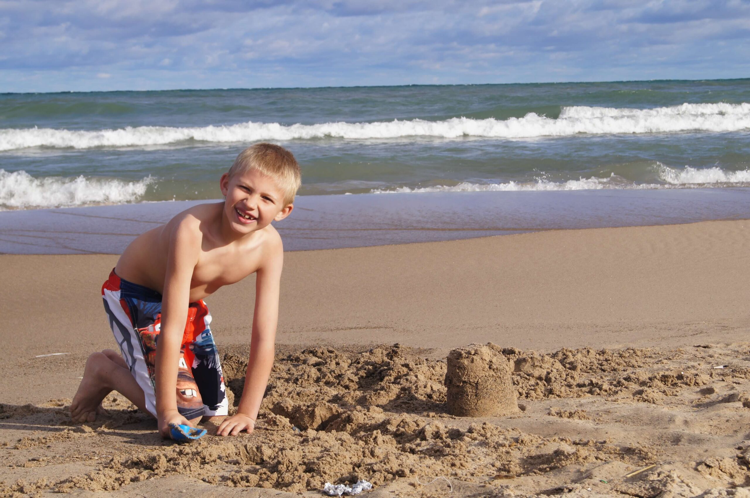 boy building sandcastle on beach with ocean waves behind