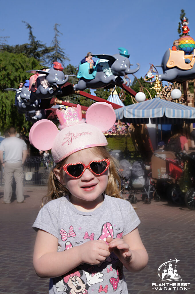 Cutel ittle girl with pink mickey ears hat in front of Dumbo the flying elephant at Disneyland California