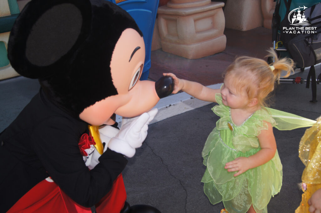 Mickey Mouse with little girl dressed as Tinkerbell who is grabbing his nose at Disneyland California toontown