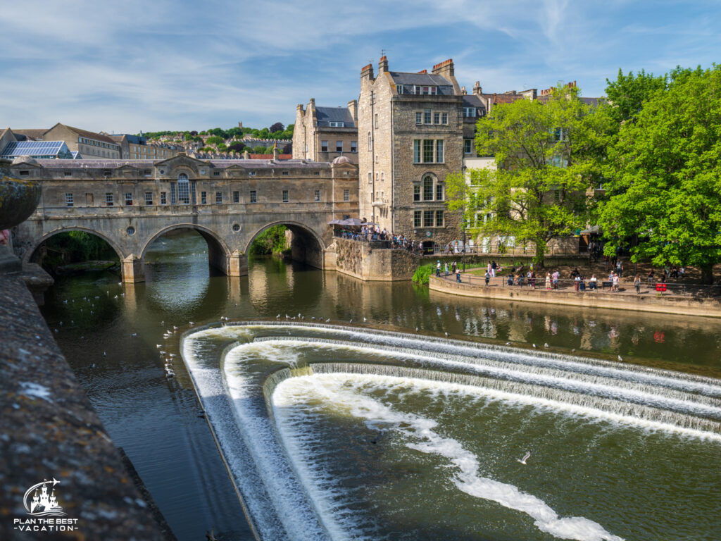 Take a scenic drive past the iconic Historic Pulteney Bridge, where charming shops line the pathway over the River. Continue your journey through The Royal Crescent, a stunning row of 30 terraced houses elegantly arranged in a sweeping crescent shape. This is one of the finest examples of Georgian architecture in the UK and a must-see when visiting Bath. Pulteney Bridge
